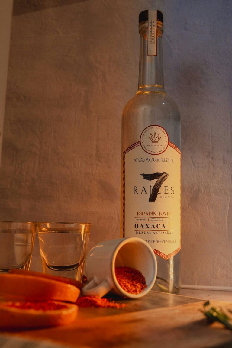 A bottle of artisanal mezcal with sliced orange and chili powder in a rustic setting.