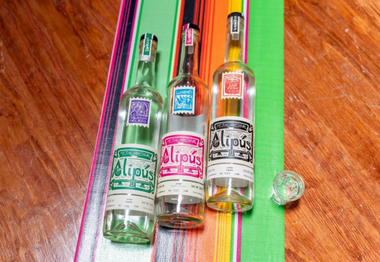 A vibrant display of Alipús mezcal bottles on a colorful Mexican tablecloth in Mexico City.